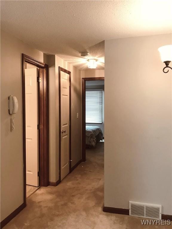 hall featuring a textured ceiling, baseboards, visible vents, and light carpet