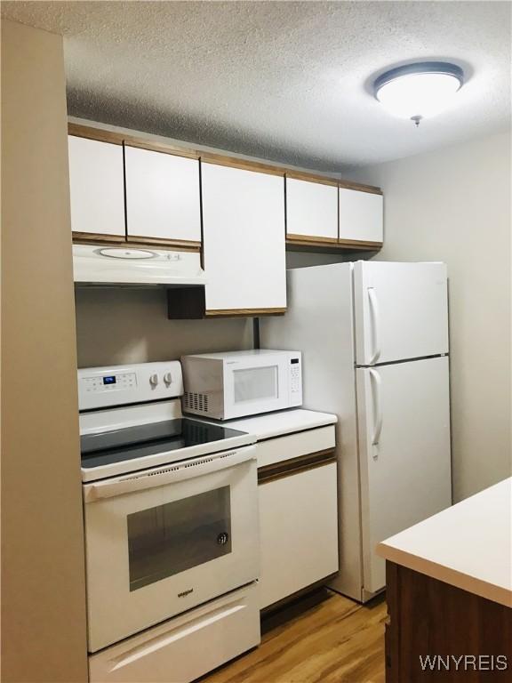 kitchen with white appliances, light countertops, light wood-style floors, under cabinet range hood, and white cabinetry