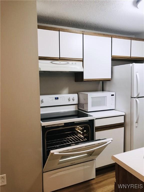 kitchen featuring white appliances, extractor fan, white cabinets, and light countertops