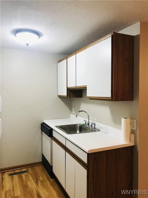 kitchen featuring light countertops, white cabinets, white dishwasher, and a sink