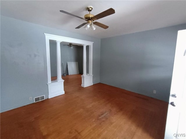 empty room with visible vents, wood finished floors, a ceiling fan, and decorative columns