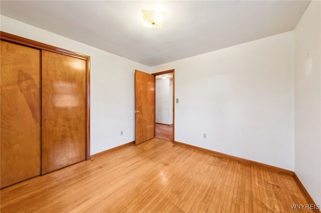 unfurnished bedroom featuring light wood finished floors, a closet, and baseboards