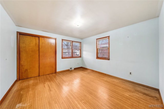 unfurnished bedroom with light wood-type flooring, visible vents, baseboards, and a closet