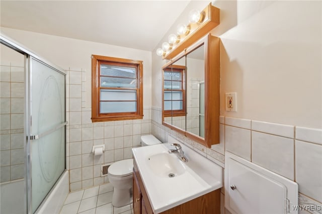 bathroom featuring toilet, shower / bath combination with glass door, tile walls, tile patterned flooring, and vanity