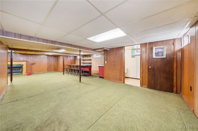 basement featuring wooden walls, a drop ceiling, a fireplace, and carpet floors