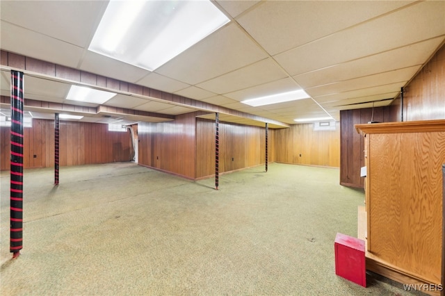 basement featuring carpet flooring, a drop ceiling, and wood walls