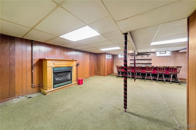 below grade area featuring wooden walls, a dry bar, carpet floors, a fireplace, and a paneled ceiling