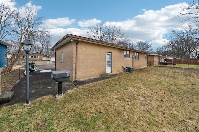 view of side of home with fence, a yard, brick siding, central AC unit, and a chimney