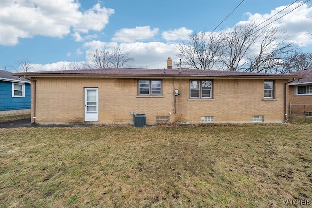 back of house with brick siding, a lawn, a chimney, and fence