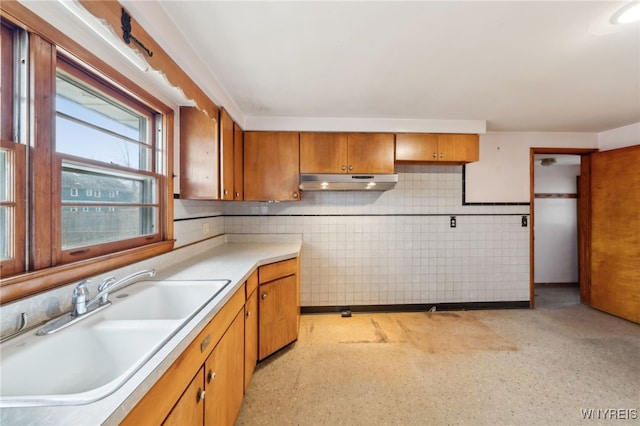 kitchen featuring under cabinet range hood, brown cabinets, light countertops, and a sink