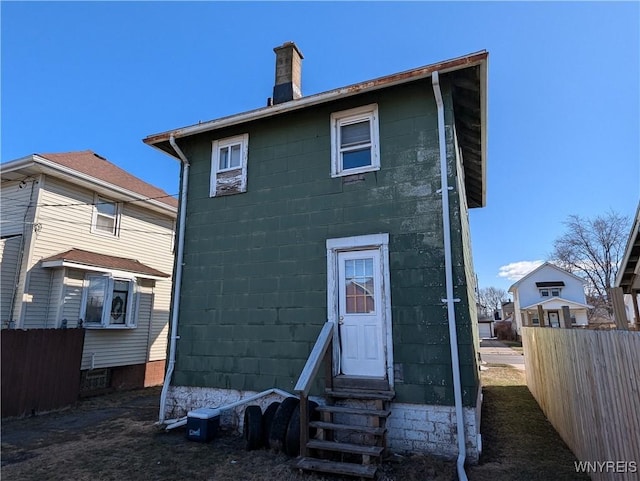 back of property featuring entry steps, concrete block siding, fence, and a chimney