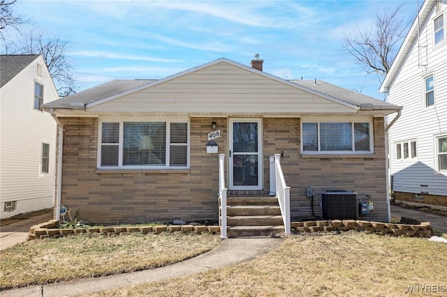 bungalow-style home with entry steps, stone siding, cooling unit, roof with shingles, and a chimney