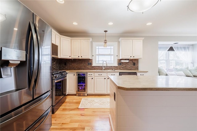 kitchen featuring a sink, stainless steel appliances, wine cooler, crown molding, and light wood-type flooring