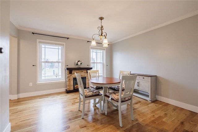 dining space featuring a stone fireplace, light wood-style flooring, and crown molding