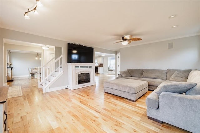 living room with baseboards, a fireplace, ceiling fan, ornamental molding, and light wood-type flooring