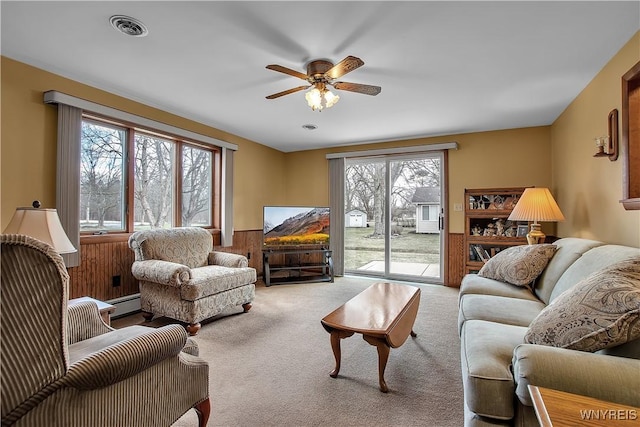 carpeted living area with visible vents, wainscoting, a baseboard heating unit, and ceiling fan