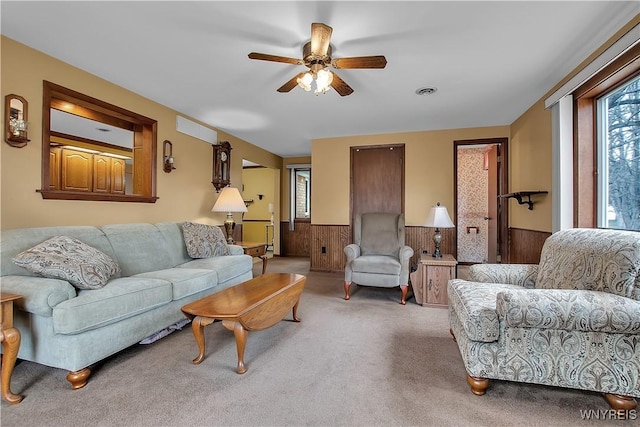 carpeted living area with a ceiling fan, visible vents, wood walls, and wainscoting