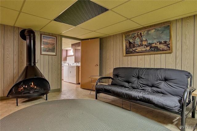 living area with a wood stove, wooden walls, independent washer and dryer, and a drop ceiling