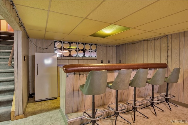 bar with light floors, freestanding refrigerator, stairs, wood walls, and a dry bar