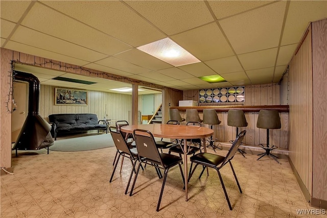 dining space featuring wood walls, a paneled ceiling, light floors, a dry bar, and stairs