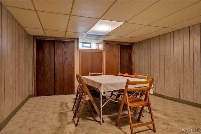 dining room featuring a drop ceiling, baseboards, light floors, and wooden walls