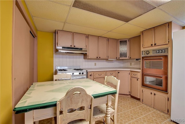 kitchen featuring double wall oven, white range with gas stovetop, light countertops, under cabinet range hood, and tasteful backsplash