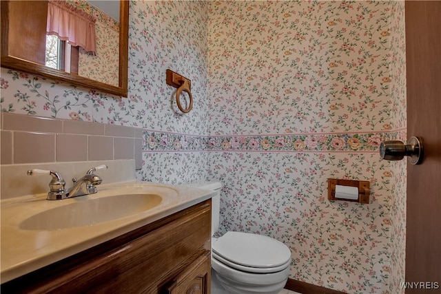 bathroom featuring toilet, vanity, and wallpapered walls