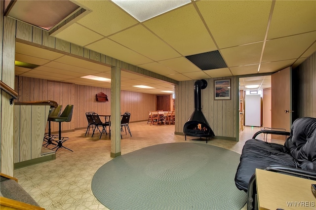 finished below grade area featuring tile patterned floors, a drop ceiling, wood walls, and a wood stove