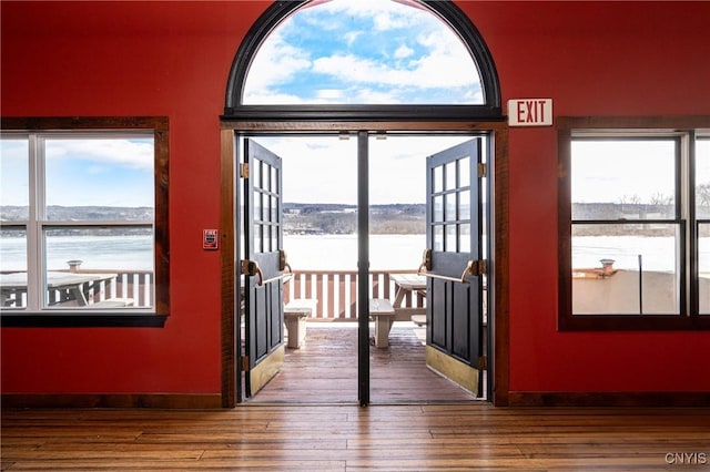 doorway with baseboards, a water view, and hardwood / wood-style flooring