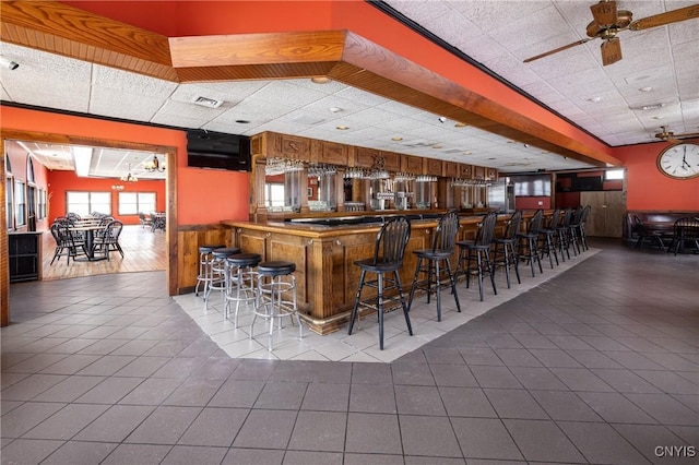 bar with tile patterned flooring, visible vents, a bar, a paneled ceiling, and a ceiling fan