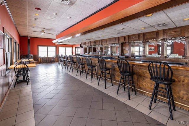 bar with tile patterned flooring, a drop ceiling, a wood stove, and a community bar