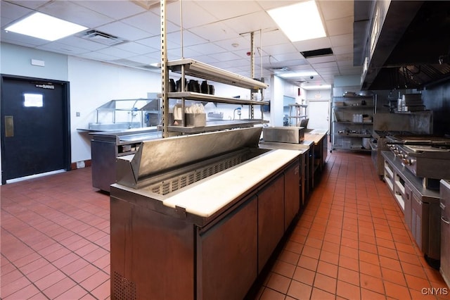 kitchen featuring tile patterned flooring, visible vents, a paneled ceiling, and wall chimney range hood