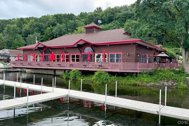 exterior space featuring a wooded view, a water view, and a shingled roof