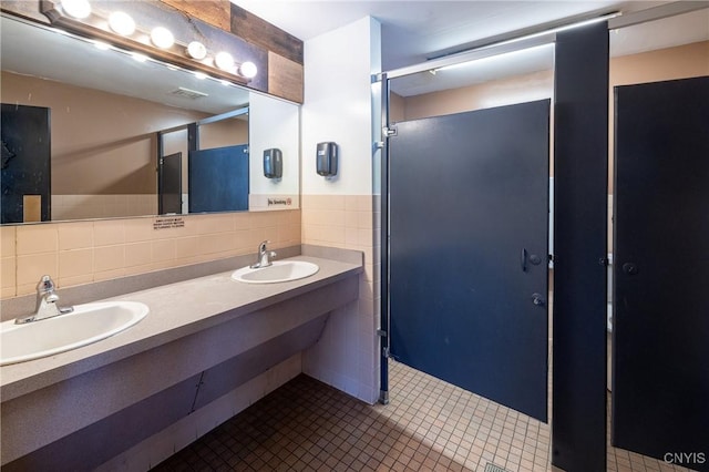 full bathroom featuring double vanity, tile patterned flooring, tile walls, and a sink