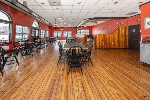 dining space featuring a drop ceiling, visible vents, wood finished floors, and wood walls