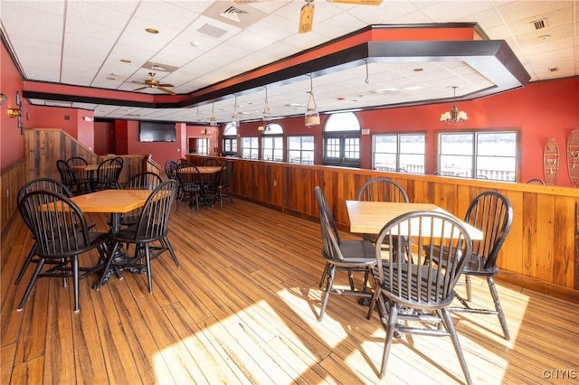 dining space with visible vents, a wainscoted wall, wooden walls, and wood finished floors