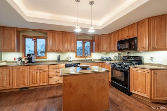 kitchen with black appliances, dark wood-style flooring, a tray ceiling, and a kitchen island