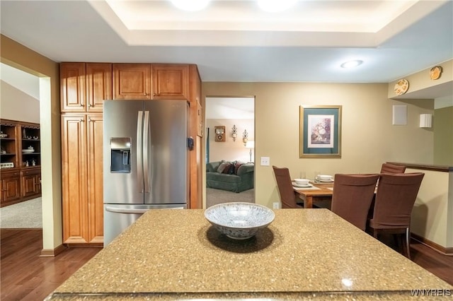 kitchen with a tray ceiling, a kitchen island, stainless steel refrigerator with ice dispenser, and dark wood-type flooring