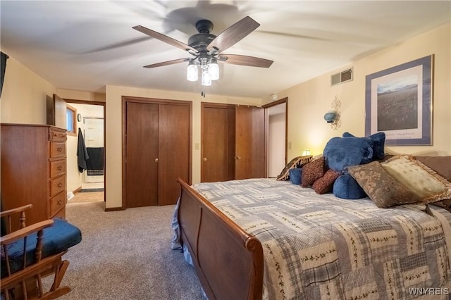 bedroom featuring visible vents, light colored carpet, multiple closets, and ceiling fan