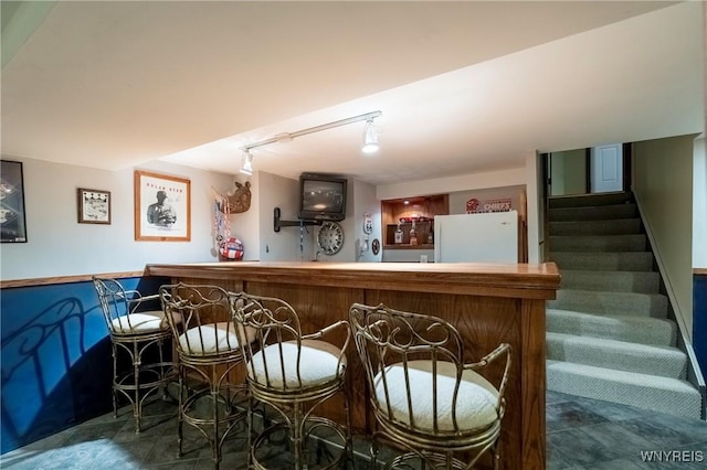 bar with a bar, track lighting, stairway, and freestanding refrigerator