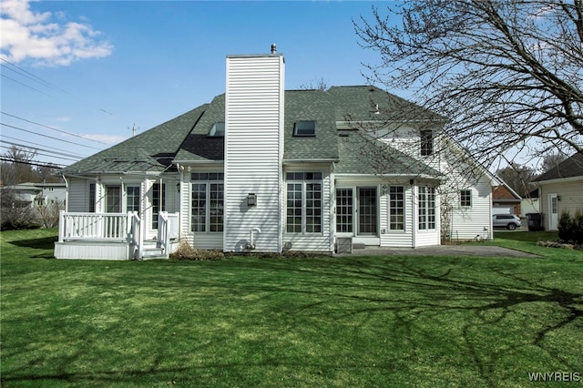 rear view of property with a patio, a lawn, a chimney, and a shingled roof