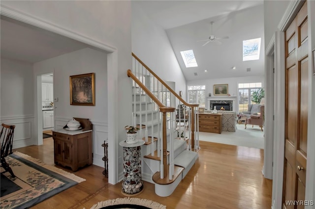 foyer with a glass covered fireplace, a skylight, wainscoting, light wood finished floors, and stairs