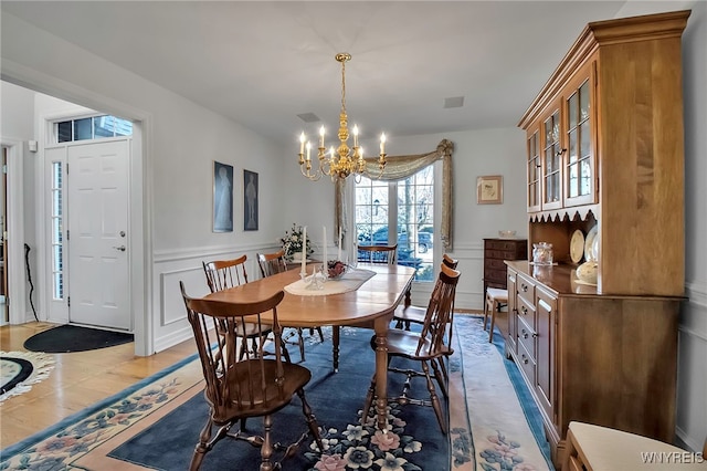 dining area with light wood finished floors, visible vents, a decorative wall, wainscoting, and a notable chandelier