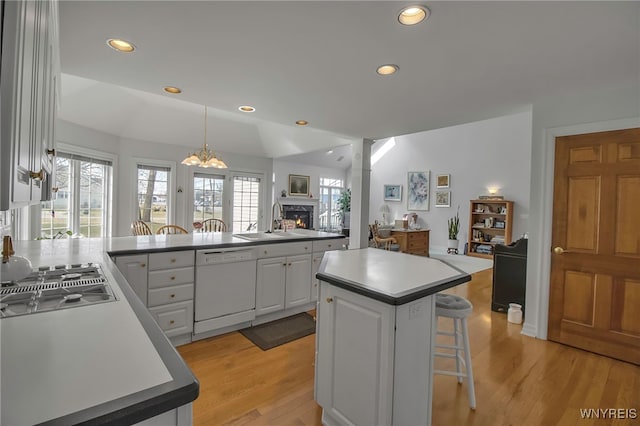 kitchen with open floor plan, dishwasher, a kitchen bar, a warm lit fireplace, and a sink