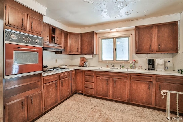 kitchen featuring oven, under cabinet range hood, a sink, light countertops, and stainless steel stovetop