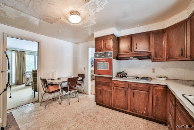 kitchen featuring oven, under cabinet range hood, stainless steel gas stovetop, light countertops, and light colored carpet