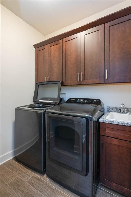 clothes washing area with wood finish floors, a sink, washing machine and dryer, cabinet space, and baseboards