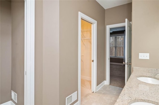 full bath with baseboards, visible vents, double vanity, a sink, and a spacious closet