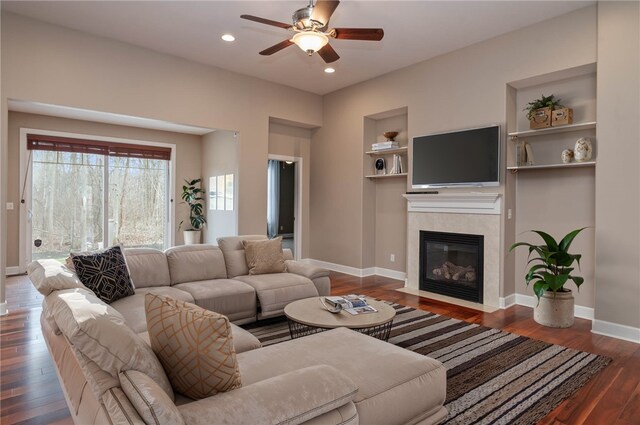 living room featuring built in shelves, a tiled fireplace, wood finished floors, recessed lighting, and baseboards