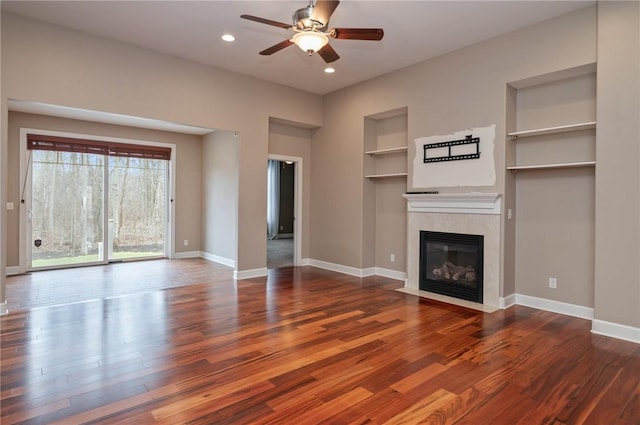 unfurnished living room with dark wood finished floors, a tiled fireplace, built in shelves, and baseboards